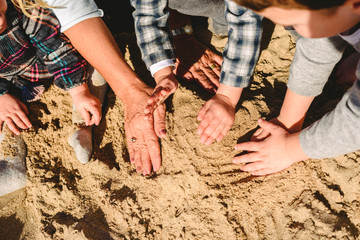 Hands of a family playing with the sand on the beach.