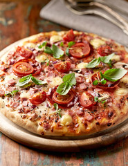 Pizza with cherry tomatoes and fresh herbs. Home made food. Concept for a tasty and hearty meal. Brown wooden background.