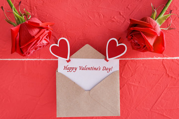 Inscription happy valentine's day on card with craft envelope on red background, roses and hearts on clothespins, closeup view
