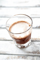 Glass of chocolate milk on bright wooden background.