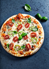 Pizza with cherry tomatoes, mozzarella cheese, jalapeno pepper, capers and fresh basil. Dark stone background. Top view.