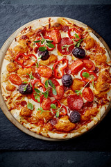 Pizza with mozzarella cheese, cherry tomatoes, black olives and fresh oregano. Home made food. Concept for a tasty and hearty meal. Black stone background. Top view. 