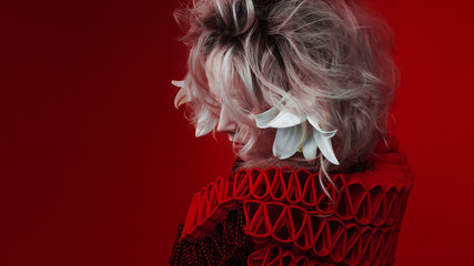 Shades of red. Attractive woman, in a red dress, posing on a red background, with white lily...