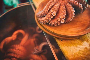 Galician octopus cooked on a wooden plate while more octopus is cooked in a metal pot