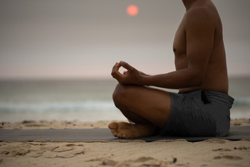 Fototapeta na wymiar Haft part of male body sitting back straight conducting Yoga Meditation on the beach with beautiful sunrising at the background 