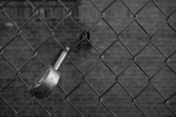 black and white closeup of old lock on chainlink fence background