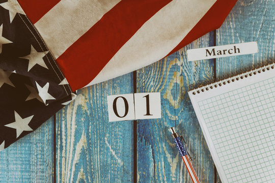 01 March calendar day Flag of the United States of America symbol of freedom and democracy with blank notepad and pen on office wooden table - Powered by Adobe