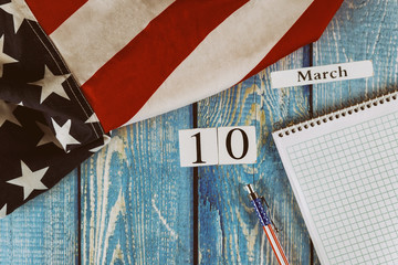 10 March calendar day Flag of the United States of America symbol of freedom and democracy with blank notepad and pen on office wooden table