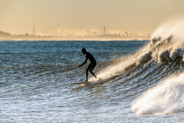 Silhouetted surfer figure drops in on a fun size wave with white water splash during golden hour on the California coast.