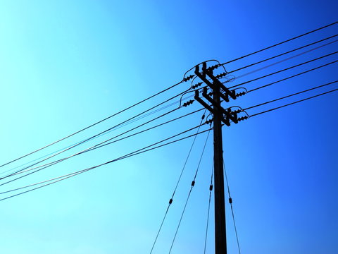 Silhouettes of pylons of high voltage cables with Guy Wire allows for tension and resistance of the pole. On a background of blue sky and the afternoon sun. With copy space for text