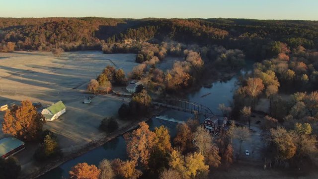 Stationary aerial view of early morning fall colors of the Ozark Mountains. This is beside the War Eagle river with working grist mill, and old iron bridge