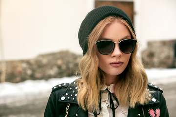 portrait of an urban girl in a leather jacket wearing sunglasses and a black hat during a...