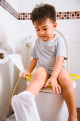 Asian little  kid 2-3 years old sitting on a kid bathroom accessory toilet