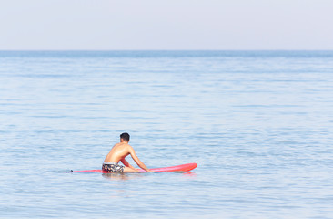 Handsome guy sitting on a surfboard in the sea