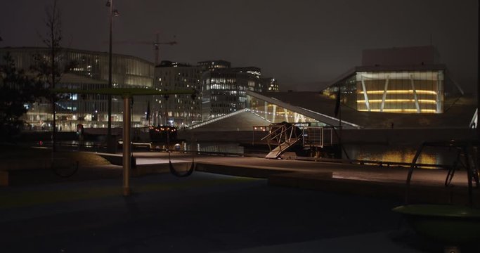 Medium full 4K professional shot with slow parallax motion of empty swings in playground with the illuminated Opera Ballet House and Edvard Munch gallery Lambda in background, at night in Oslo Norway.