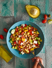 Top view of East Balela salad with chickpea, avocado, feta cheese, cherry tomato, onions and herbs on a blue background, person eating a salad, mediterranean cuisine