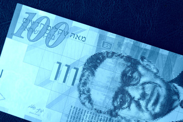 One hundred shekels banknote on a dark background close-up. Money background blue color toned