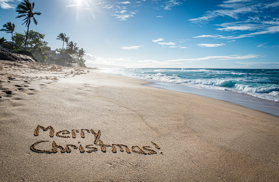 Merry Christmas written in the sand on Sunset Beach in Hawaii with palm trees and the ocean in the background