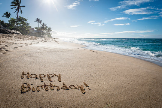 Happy Birthday written in the sand on Sunset Beach in Hawaii with palm trees and the ocean in the background