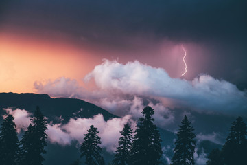 Lightning strike on the dark cloudy sky at the sunset at the mountain.