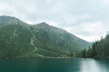 Landscape of a mountain lake with blue water in the rain with a wooden tourist house. Lake Morskie Oko, view of a wooden house. Tatra Mountains. Background.