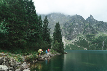 Group of tourists in raincoats walk along a stone path near a mountain lake ,backdrop of beautiful rocky mountains. Landscape trails with beautiful views near Lake Morskie Oko in the Tatra Mountains