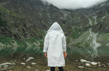 Portrait from back of person in white raincoat on background of beautiful lake on top of mountain. Background. Man hiking in the mountains. Man and untouched nature concept.