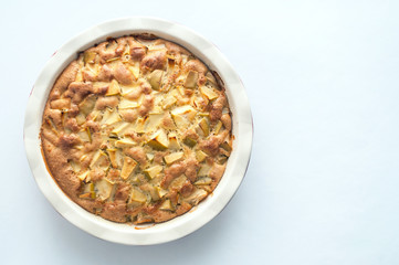 Homemade baked apple cake in a white round ceramic baking dish on a white background, top view