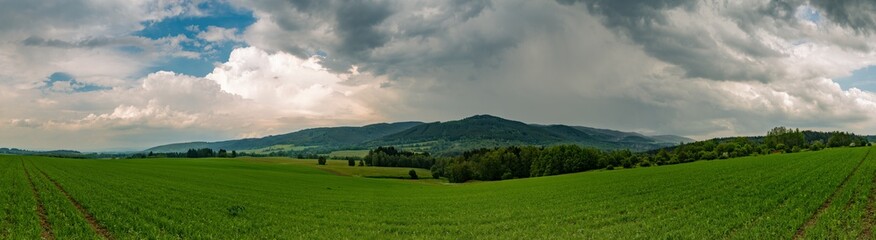 Fototapeta na wymiar panorama of landscape with hills, trees and green fields and storm clouds