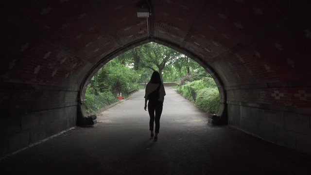 Lady walking under a tunnel and into central park in New York City. This was taken at a regular speed with natural motion blur.
