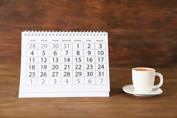 Calendar and cup of coffee on wooden table