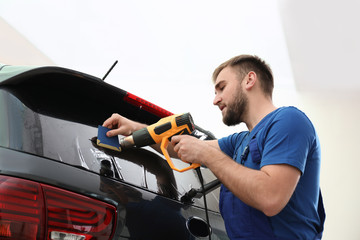 Worker tinting car window with heat gun in workshop