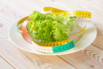 Photography of measuring tape on white plate with green salad leaves. Dieting concept image