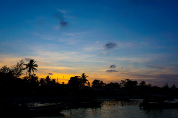 Silhouette of boat and fisherman village in blue and orange sunset background,soft focus
