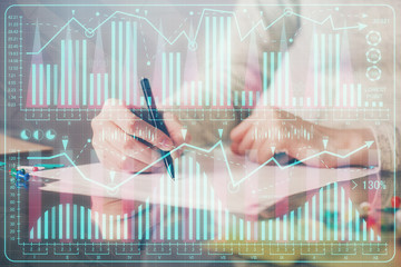 Hand taking notes in notepad. Forex chart holograms in front. Concept of research. Multi exposure