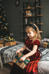 Fototapeta na wymiar Happy little girl with gift box sitting on bed. Child having fun in Christmas time.
