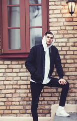 cool men in jeans, jacket and white sneakers against a brick building