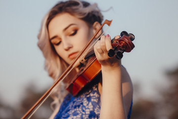 Fototapeta premium face of a beautiful girl with a violin under her chin outdoors, romantic young woman playing a musical instrument on nature in solitude, concept music and feelings