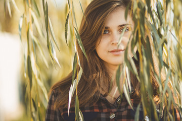 portrait of a beautiful romantic girl looking out of willow branches and foliage in autumn, the face of a young woman looking at you in in nature © fantom_rd