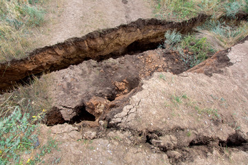 landslide in an environmentally hazardous area large crack in ground descent of large layers of soil close up top view.