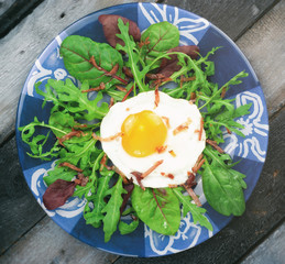 Fried egg with bacon and mixed salad on wooden table.