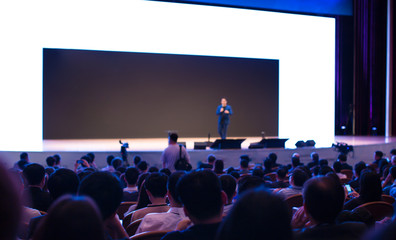 Speaker on the stage with rear view of audience in the conference hall or seminar meeting, business...