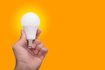 Hand holding an light bulb isolated on orange background