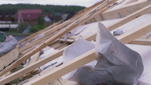 Side view of unfinished roof covered by white roofing material with fireproof effect. Clip. Close up of wooden boards and white fabric at the construction site.