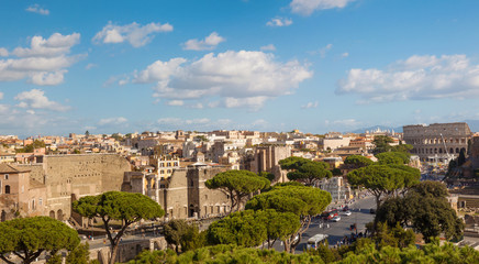 Fototapeta na wymiar Horizontal panoramic view of the landscape of Rome with a view of the Colosseum, the road with cars, ancient ruins, green pine trees, blue sky with large clouds. Aerial view, Italy