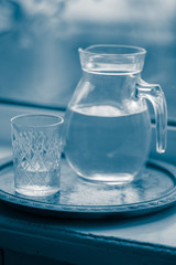 Jug of water and a glass on the windowsill, blue tone.