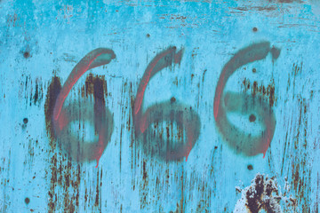 No. 666. The number three sixes in red paint on an old rusty blue surface. Number six hundred sixty six on a ragged metal surface.