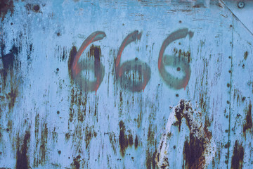 No. 666. The number three sixes in red paint on an old rusty blue surface. Number six hundred sixty six on a ragged metal surface. Copy space.