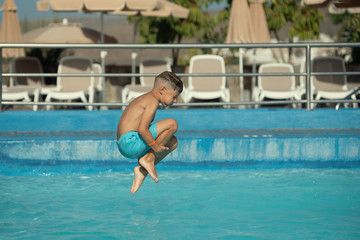 Caucasian boy having fun running to make jump into swimming pool at resort.  He is enjoying his...
