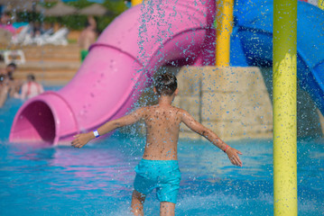 Active Caucasian boy spending his summer holidays in water park, he splashing in pool against...